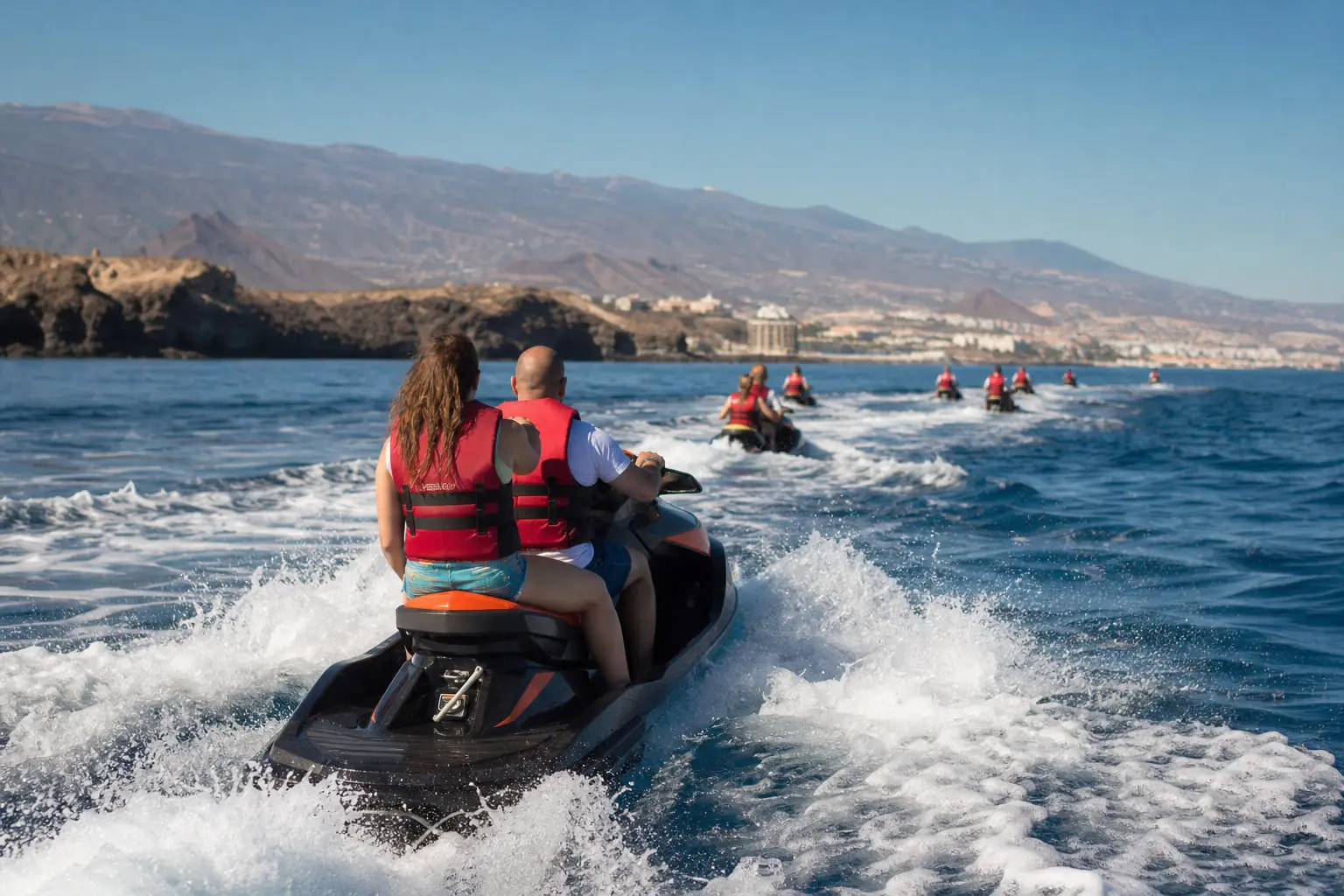 Jet ski en navigation encadrée le matin au large de Costa Adeje à Tenerife, avec la côte volcanique en arrière-plan.