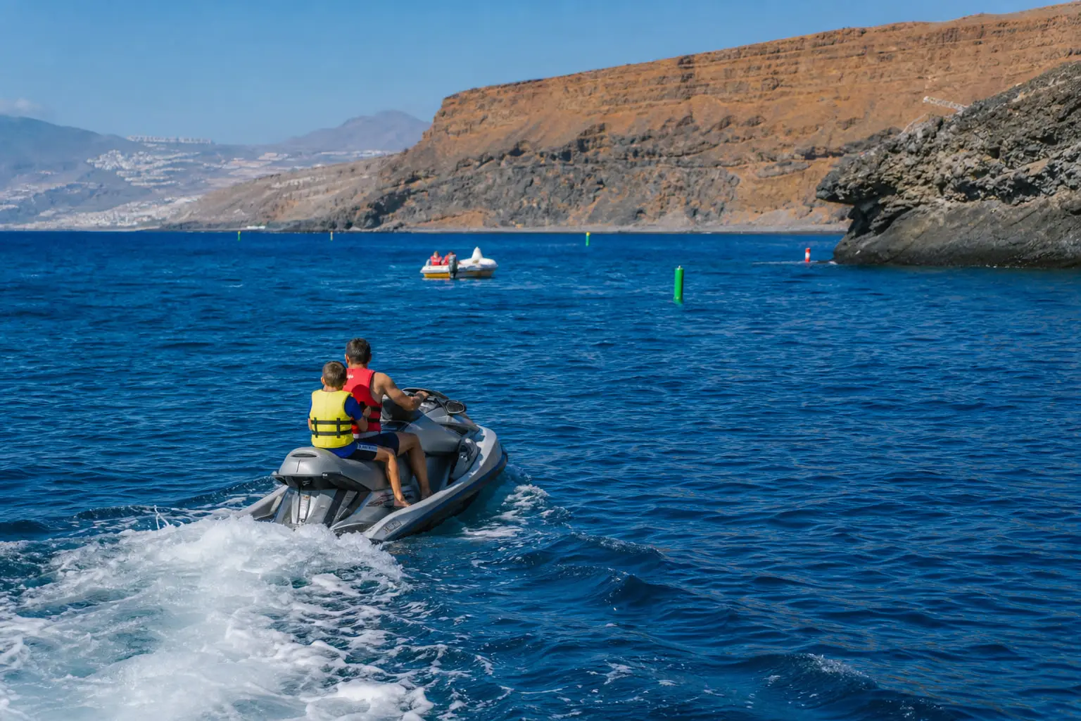 Un adulte et un enfant portant des gilets de sauvetage sur une moto nautique, au large de Costa Adeje à Tenerife, par mer calme le matin.