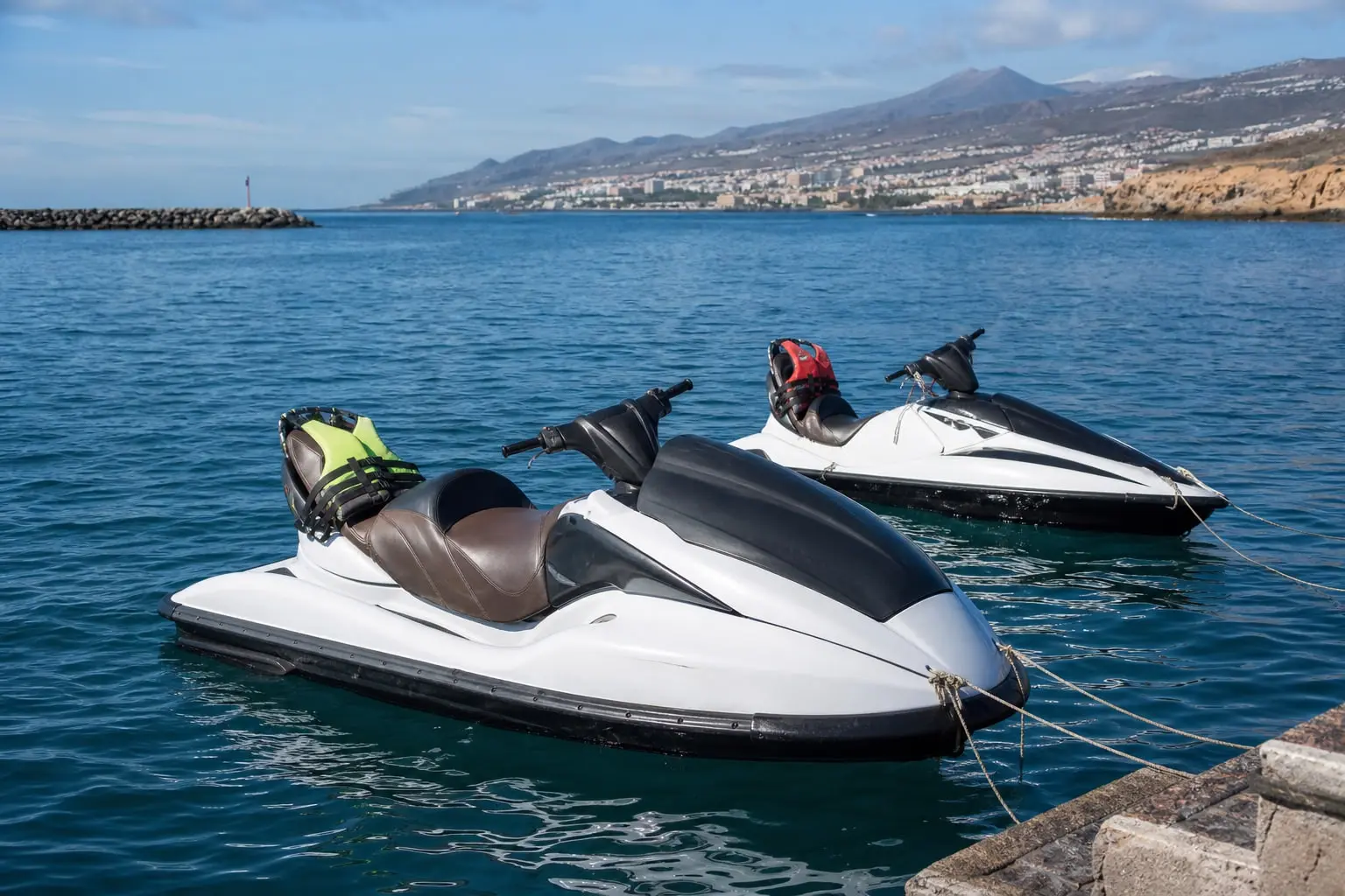 Jet ski de loisir trois places naviguant le matin au large de la côte sud-ouest de Tenerife, avec une moto nautique sportive au loin.