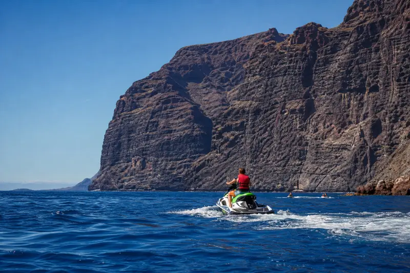 Deux jet skis espacés naviguent le matin au large de la côte sud-ouest de Tenerife, avec les falaises de Los Gigantes en arrière-plan.