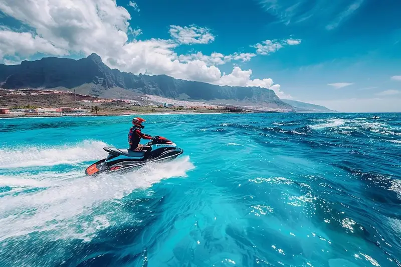 Groupe de jet skis suivant un moniteur au large de la côte sud-ouest de Tenerife, avec des falaises volcaniques au loin.
