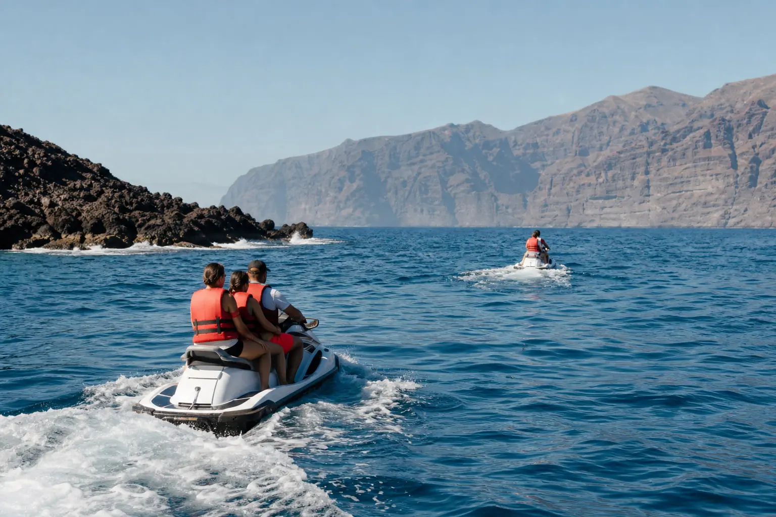 Jet ski naviguant le matin au large d’une côte volcanique de Tenerife, loin des rochers et des falaises.
